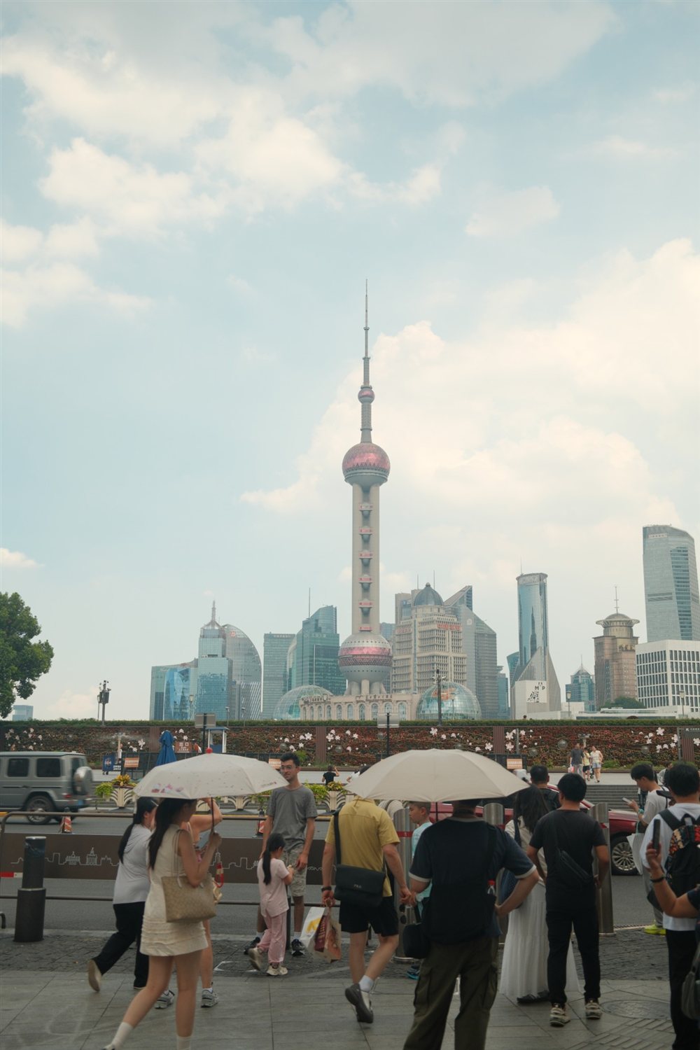 The Oriental Pearl Tower and Pudong skyline behind people with umbrellas on the Bund